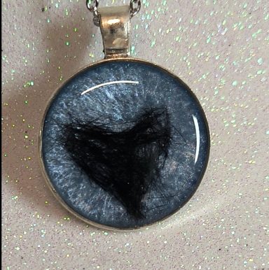 Collar con un colgante circular que presenta un corazón negro sobre un fondo gris.